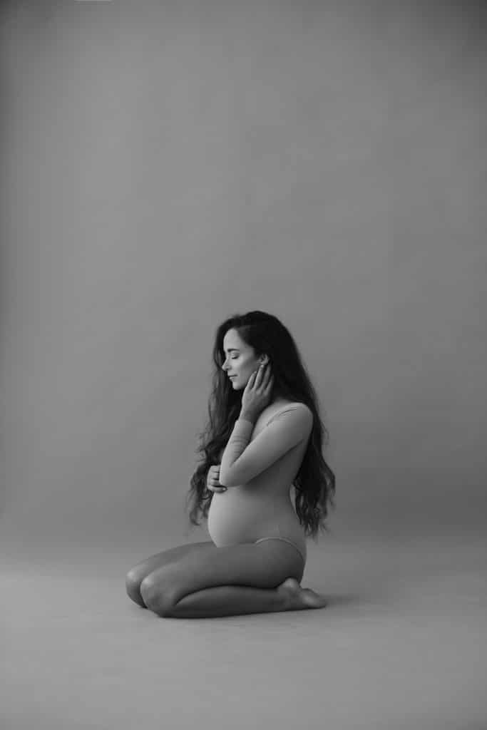 Black and white photo of beautiful pregnant woman with long curly hair sitting on a floor.
